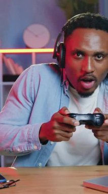 30 yaşında, video oyunlarında zafer kutlamalarında kameraya neşeli bir yüz ifadesiyle poz veren kablosuz kulaklıklı Afro-Amerikan oyuncu portresi.
