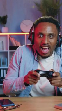 Çekici duygusal ruh hali iyi 30 yaşında, kablosuz kulaklıklı Amerikalı erkek oyuncu akşamları evde tek başına eğleniyor ve hayal kırıklığına uğruyor çünkü kaybediyor.