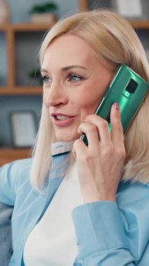 Hoş, gülümseyen, tasasız, açık renk saçlı bir kadının portresi modern dairede rahat bir kanepede rahat rahat sohbet ediyor.