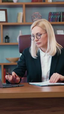 İyi donanımlı bir iş yerinde masada oturan ve bilgisayardan mali belgelere veri yazan, kasten nitelikli iş kadını portresi.