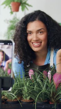 Önlüklü Afrikalı Amerikalı kadın çiçekçi çiçekçide telefon kullanarak video çekiyor. Güzel kadın bahçıvan takipçiler için canlı konferans düzenliyor. Çiçekçilik ve modern teknoloji konsepti. Küçük işletme kavramı.