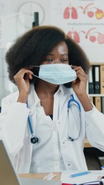 Tıp konsepti, 30 yaşında, sevimli, yüksek yetenekli Afro-Amerikan kadın hemşirenin tıp laboratuarında kameranın önünde oturması ve internette salgın sırasında tıbbi maske takması gerektiğini açıklaması.