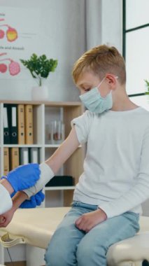 Güzel görünümlü, koruyucu maskeli, tendonu hasarlı ve ellerini elastik bandajla saran, maskeli, ne kadar çekici, attantif, kadın-tıp çalışanı bir arada izlediği için muayene maskesinde oturan sakin bir gencin ön görüntüsü.