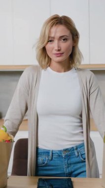 Çekici kadın şefin portresi kamera karşısında gülümseyerek mutfaktaki kese kağıdının yanında taze sebzelerle dolu. Yavaş çekim.