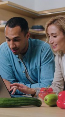 Afrikalı erkek ve kadın iyi haberleri dizüstü bilgisayardan okuyorlar. Çok ırklı çift mutfakta dizüstü bilgisayarlı e-postalarla oturup evet işareti yaparak zaferi kutluyorlar. Yavaş çekim.