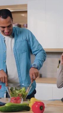 Evde birlikte mutlu bir aile. Gülümseyen kadın, modern mutfakta kocasıyla telefonda konuşuyor ve salata pişiriyor. Evde birlikte mutlu bir aile. Yavaş çekim.