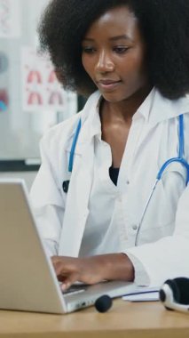 Büyüleyici pozitifliğin portresi 30 yaşında, beyaz önlüklü Afro-Amerikan kadın-sağlık görevlisi modern çalışma odasındaki bilgisayarda daktilo yazarken sakallı adam telefonu kullanıyor.