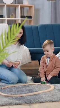 Çekici siyah saçlı genç anne en küçük oğlu için araba pisti toplamaya yardım ederken en büyük iki oğlu tahta bloklarla kule inşa ediyor.