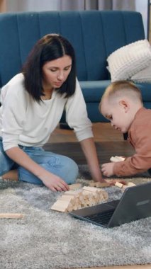 Tüylü halıda oturan ve dağınık ahşap tuğlaları iki yaşındaki oğluyla birlikte toplayan güzel, mutlu, sevgi dolu esmer kız.