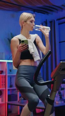 İyi görünümlü sporcu zayıf, 25 yaşında, antrenman kıyafetleri içinde bisiklet eğitmeninin pedallarını çeviren ve akşamları evdeki temiz suyla su dengesini yeniden kuran sarışın.