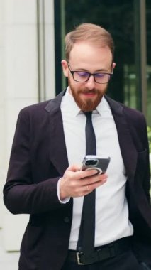 Yakışıklı genç işadamı ofis yakınlarındaki caddede yürürken cep telefonundan mesaj atmış. Sosyal ağ. - İnsanlar. Uygulamalar. Yavaş çekim.