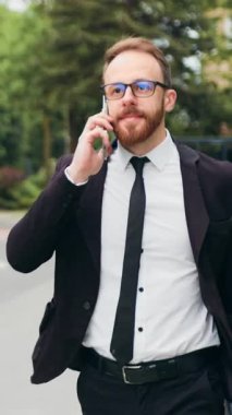 Portre yakışıklı adam ofis merkezinin yakınından telefon görüşmesi yapıyor. İş adamı sokakta akıllı telefondan konuşuyor. İşten eve yürüyerek dönen bir erkek uzun bir iş gününden sonra cep telefonuyla sohbet ediyor. Yavaş çekim.