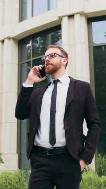 Başarılı genç işadamı iş çıkışı açık havada arama yapmak için cep telefonu kullanıyor. Şehir merkezindeki sokak röportajında akıllı telefon durağında konuşan bir adam var. Yavaş çekim.