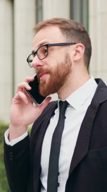 İş adamı ofis binasının yakınında cep telefonuyla konuşuyor. Dışarıda akıllı telefonlardan konuşan bir adam kaygısız konuşma iş görüşmesi iletişim konuşmaları. İş ve teknoloji kavramı. Yavaş çekim.