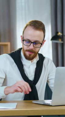 İyi görünümlü, deneyimli, sakallı, gözlüklü, güzel dekore edilmiş bir odada bilgisayar ekranında dokümanlar ve verilerle çalışan bir ofis yöneticisi.