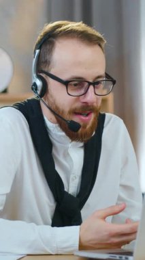 İyi bir ruh hali içinde, 30 yaşında, sakallı, kulaklıklı bir ofis çalışanı eşleri veya iş arkadaşlarıyla video görüşmesi yapıyor ve onlarla ortak çalışma konusunu tartışıyor.