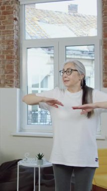 Güzel, gülümseyen, 70 yaşında, sakallı bir adam ve spor üniformalı karısı evde antrenman yaparken esneme egzersizleri yapıyorlar.