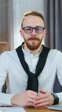 İyi görünümlü, yetenekli, 30 yaşında, kameraya poz veren ve modern odanın arka planında iyi niyet gösteren gözlüklü bir ofis müdürünün portresi.