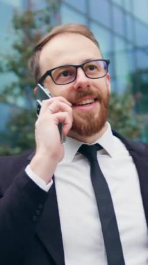 Takım elbiseli ve şık gözlüklü bir işadamı akıllı telefondan ararken şehir caddesinde duruyor. Ofis binasının yakınında cep telefonuyla konuşan başarılı bir adam. Yavaş çekim.