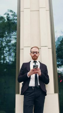 İşletme tarzı takılan ve cep telefonuyla kayan bir adam. Açık havada. Genç işadamı cep telefonu kullanıyor. Gülümsüyor. Açık havada takım elbise giyiyor. Yavaş çekim.