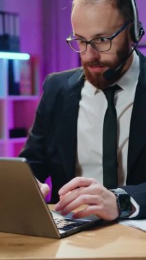 İş zaferi, güzel görünümlü, mutlu, mutlu, başarılı, sakallı, kablosuz kulaklıklı genç ofis müdürünün akşam ofisinde bilgisayarın önünde oturduğu ve monitörde inanılmaz bilgiler gördüğü yer.