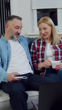 Güzel görünümlü, neşeli, sarışın bir kadın ve sakallı kocasının evdeki rahat koltukta dinlendiği ve bilgisayardaki ilginç videoyu gözden geçirdiği aile eğlencesi.