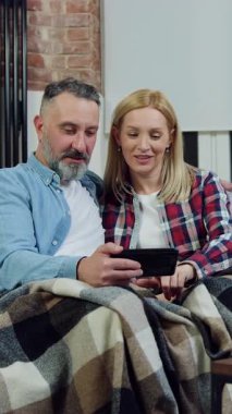 Güzel görünümlü, şehvetli, yaşlı, sakallı bir adam ve güzel, neşeli karısı kendi dairesindeki koltukta dinleniyorlar ve telefondaki özel fotoğrafları gözden geçiriyorlar.