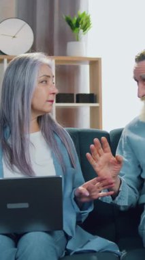 Çekici, mutlu, yetmiş yaşında erkek ve kadın oturma odasındaki rahat koltukta dinleniyor ve diz üstü bilgisayardan son dakika haberleri okurken gözleri kapalı meditasyon yapıyor.