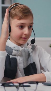 Yakından bakınca, sevimli çocuk elini kaldırıyor ve cevapları veriyor. Kulaklıklı bir çocuk bilgisayar laptopuyla evde online okul dersine katılıyor. Yavaş çekim.