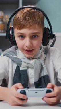 Heyecanlı küçük çocuk portresi masada oturuyor, duygusal olarak konsolda oynuyor, oyunu kaybediyor, mağlubiyet duygusunu. Mutlu çocuk iyi eğlenceler. Okuldan sonra evde oyun bağımlılığı konsepti. Yavaş çekim.