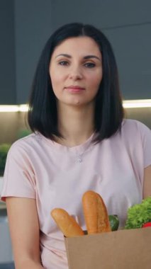 Çağdaş mutfak arka planında büyük bir kese kağıdıyla kameraya poz veren muhteşem gülümseyen genç esmer.