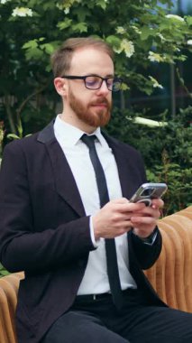 Genç işadamı iş bölgesinde bankta otururken verileri analiz ediyor. Yakışıklı erkek e-postaları kontrol ediyor, internette sohbet ediyor, müşteriyle mesajlaşıyor, sosyal medyada geziniyor. Yavaş çekim.