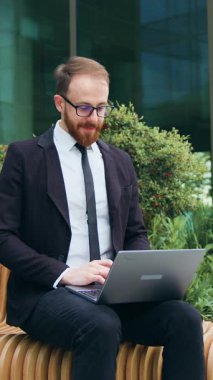 Sırıtkan sakallı iş adamı dışarıda dizüstü bilgisayarla bankta çalışıyor. Gözlüklü bir serbest çalışan, şehir sokağında uzaktan çalışmayı öğreniyor. Yavaş çekim.