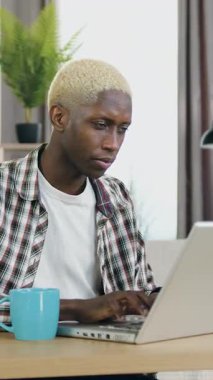 Çekici, kendine güvenen, 25 yaşında, modaya uygun, rahat bir odada oturan ve bilgisayarda yazı yazan Afrikalı Amerikalıların portresi.