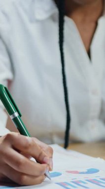 Başarılı başarılı bir profesyonel Afro-Amerikan kadın iş adamı şık giyiniyor laptop ekranına tarama verileri takıyor ve karanlık zamanlarda modern çalışma odasında gerekli notları kağıda döküyor.