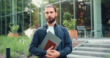 Modern ofis binasının önünde dikilirken kameraya gülümseyen gözlüklü bir iş adamı. Şık giyinmiş pozitif erkek portresi.