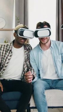 Homoseksüel ilişki ve 25 yaşındaki kaygısız erkek aşıkların birleşimi. Oturma odasında çapraz parmaklarla kanepede oturan ve arttırılmış gerçeklik gözlüğü kullanan erkekler.