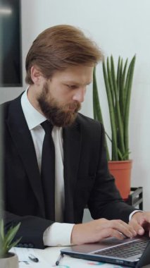 Çekici, kendine güvenen, başarılı, sakallı, iş yerinde oturan ve kağıt raporundan ve bilgisayardan yavaş çekimde bilgi okuyan başarılı bir iş adamı.