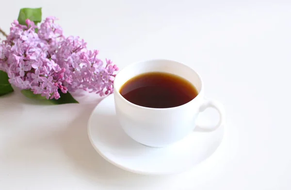 Romantische achtergrond met een kopje koffie met een takje lila op witte tafel. Zachte foto. Wenskaart. Bovenaanzicht plat lag met kopieerruimte. — Stockfoto