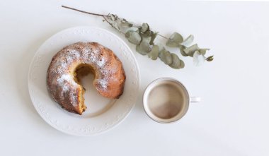 Close up of delicious homemade bundt cake dessert and fresh coffee on a white table background with a twig of eucalyptus.Top view. Food concept.