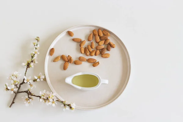 Virágzó mandula gallyak maceráló mandula olaj, hogy készítsen egy bőr tonik, cserépedény lemez és fehér asztal háttere.Spa termékek. Stock Fotó