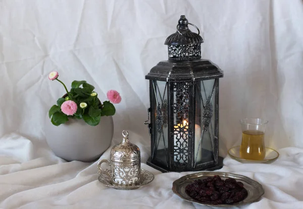 Een zilveren decoratieve kop thee, bloemen en gloeiende Marokkaanse lantaarn op een witte achtergrond. Een teerdiner. Ramadan Kareem wenskaart, uitnodiging. Eid ul Fitr Moslim vakantie. — Stockfoto