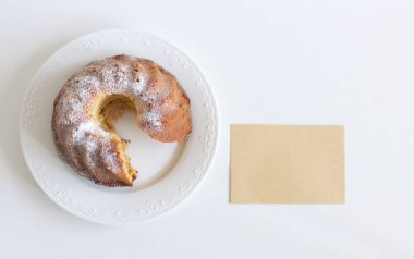 Yemek sahnesi. Beyaz masa arkaplanındaki leziz ev yapımı sünger keki ve boş tebrik kartını kapat. Düz kadın, üst görünüm.