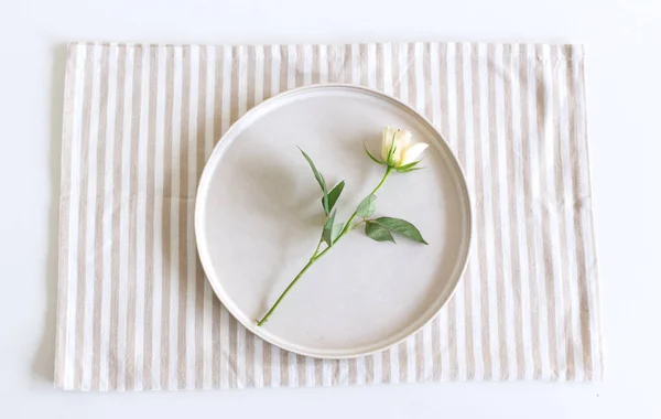 Slavnostní nastavení stolu. Prázdný talíř, ubrousek a bílá růže na bílém stole. Horní pohled, plochá poloha, kopírovací prostor. — Stock fotografie