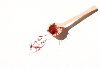 Sonbahar durgun hayat sahnesi. Crocus sativus, genellikle safran çiçeği olarak bilinir, beyaz arka planda, güneş ışığında, tahta kaşıkta kırmızı lekeler. Uzun, sert gölgeler. Yüksek açı. Doğa konsepti.