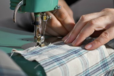 Eski bir dikiş makinesinin 30 santimlik yakın çekimi ve kadın eli. Dikiş işlemi. Ev hobisi, yaratıcılık, eğlence.