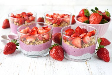 Beyaz arka planda chia pudingi, granola ve çilekli tatlı.