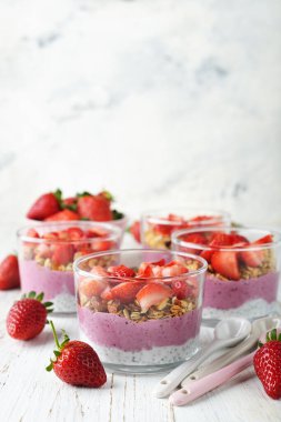 Beyaz arka planda chia pudingi, granola ve çilekli tatlı.