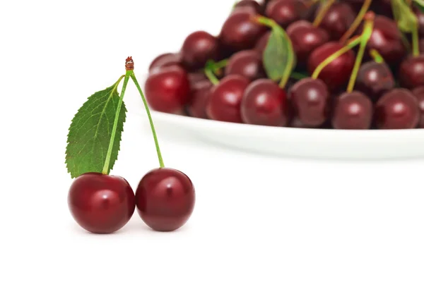 Two ripe berries with green leaf and plate of cherry (isolated) — Stock Photo, Image