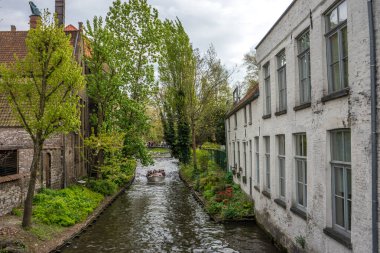 Turistler mavi gökyüzü ile aydınlık bir yaz gününde Belçika, Bruges 'de bir kanalda tekne turuna çıkarlar.
